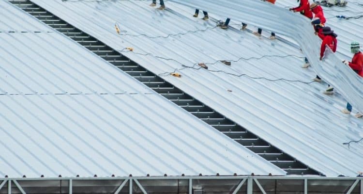Professional commercial metal roof repair crew sealing joints on a corrugated metal panel system